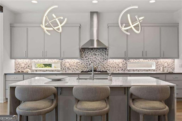 kitchen featuring tasteful backsplash, stainless steel gas cooktop, hanging light fixtures, wall chimney exhaust hood, and gray cabinets