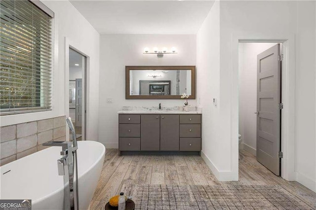 bathroom with hardwood / wood-style floors, toilet, a tub to relax in, and vanity