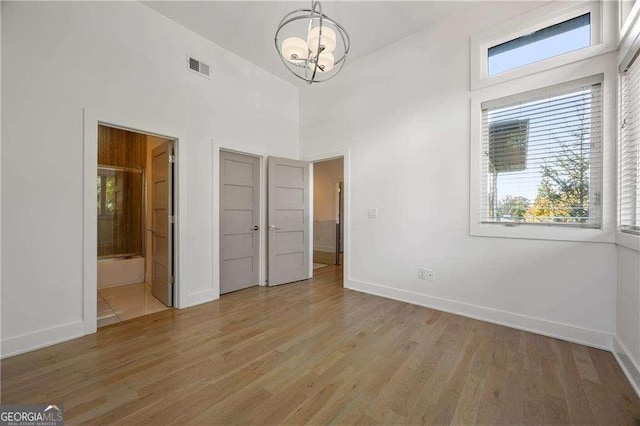 unfurnished bedroom with a chandelier, connected bathroom, light hardwood / wood-style flooring, and a towering ceiling