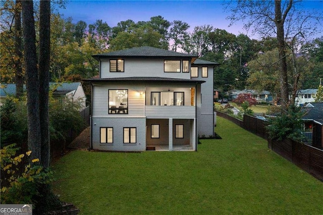 back house at dusk featuring a lawn