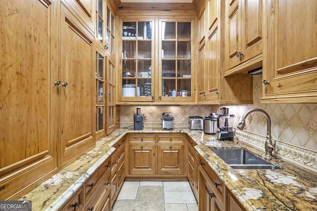 5200 Moore Rd, Suwanee, GA 30024 - kitchen featuring a sink, backsplash, brown cabinets, light stone counters, and glass insert cabinets
