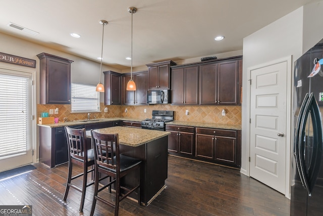 kitchen with black appliances, a kitchen island, a kitchen bar, hanging light fixtures, and dark brown cabinets