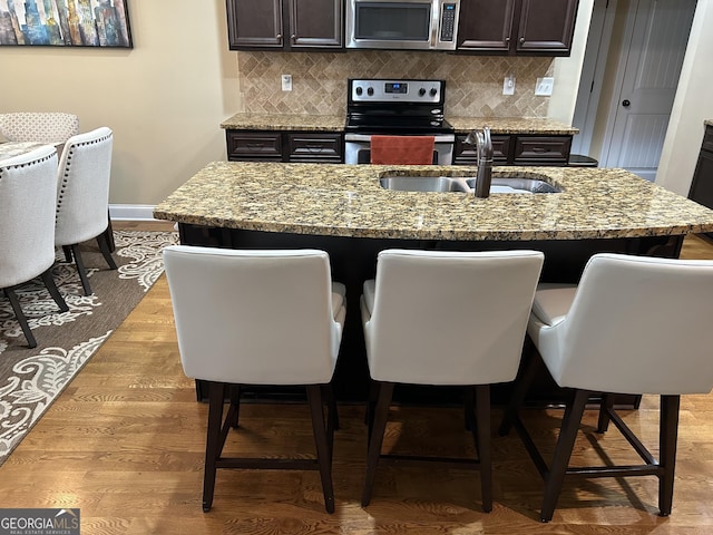 kitchen with a kitchen bar, sink, light stone counters, appliances with stainless steel finishes, and a kitchen island with sink