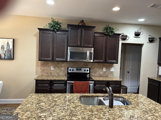 kitchen featuring sink, dark brown cabinets, stainless steel appliances, tasteful backsplash, and light stone countertops