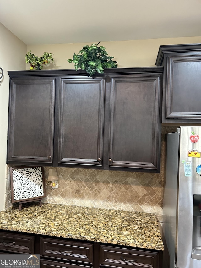 kitchen with dark brown cabinetry, stainless steel fridge, backsplash, and stone counters