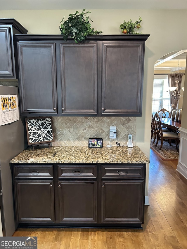 kitchen featuring stainless steel refrigerator, light stone countertops, light hardwood / wood-style floors, and decorative backsplash