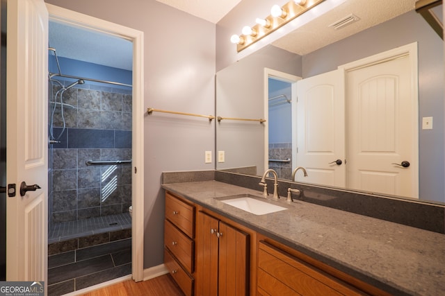 bathroom with wood-type flooring, tiled shower, and vanity