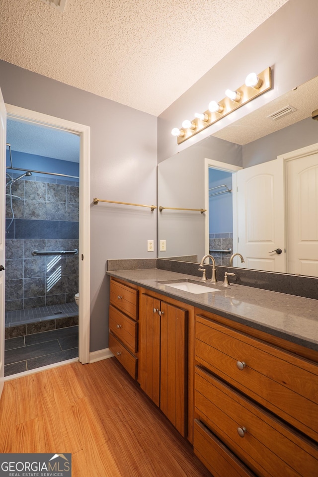 bathroom featuring wood-type flooring, toilet, a textured ceiling, walk in shower, and vanity