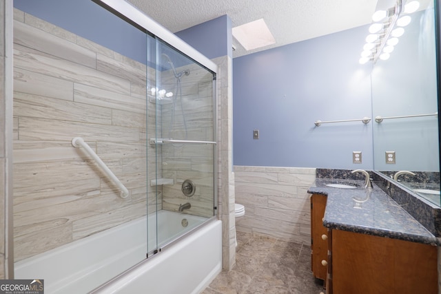 full bathroom with toilet, a textured ceiling, bath / shower combo with glass door, tile walls, and vanity