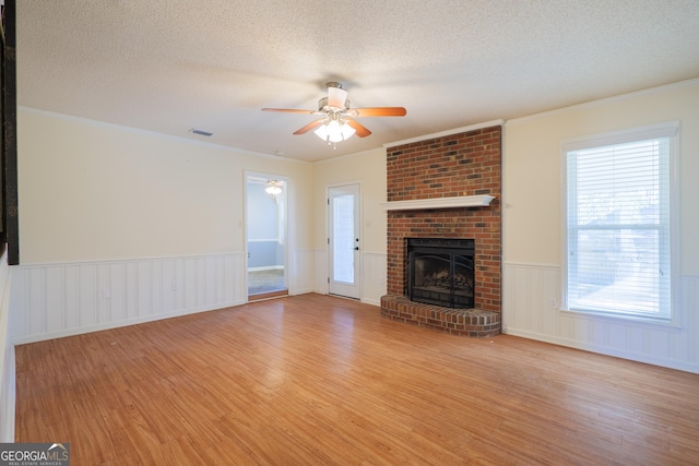 unfurnished living room featuring crown molding, light hardwood / wood-style flooring, ceiling fan, a fireplace, and a textured ceiling