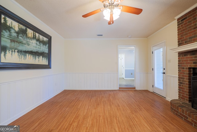 unfurnished living room featuring light hardwood / wood-style flooring, ceiling fan, a brick fireplace, a textured ceiling, and ornamental molding