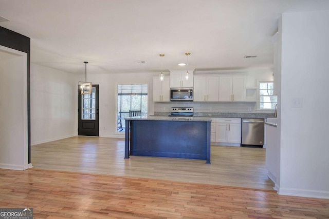 kitchen with white cabinetry, stainless steel appliances, hanging light fixtures, and light hardwood / wood-style flooring