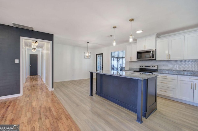 kitchen featuring pendant lighting, appliances with stainless steel finishes, a kitchen breakfast bar, a center island, and white cabinets