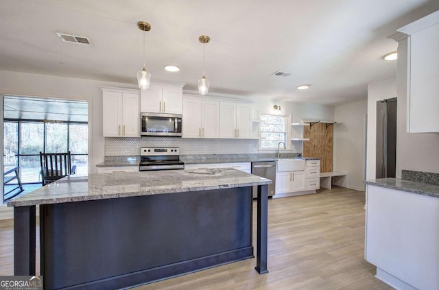 kitchen featuring hanging light fixtures, stainless steel appliances, light stone countertops, decorative backsplash, and white cabinets