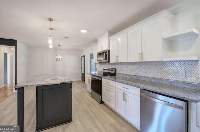 kitchen with pendant lighting, stainless steel appliances, light stone counters, white cabinets, and a kitchen island