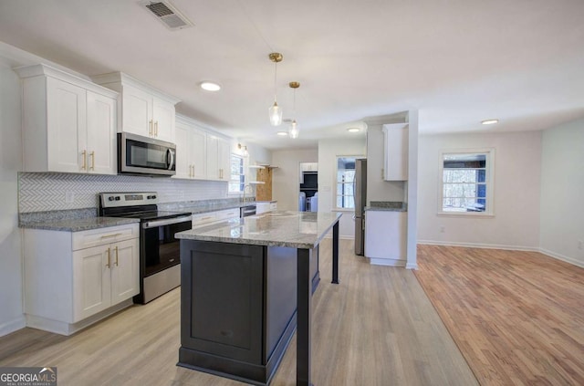 kitchen with pendant lighting, light hardwood / wood-style flooring, appliances with stainless steel finishes, white cabinetry, and light stone countertops