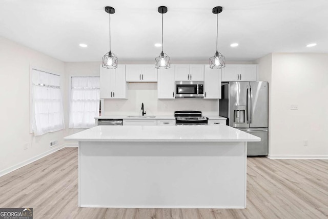 kitchen with appliances with stainless steel finishes, white cabinetry, hanging light fixtures, sink, and a kitchen island