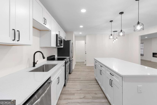 kitchen with white cabinetry, sink, decorative light fixtures, light hardwood / wood-style flooring, and stainless steel appliances