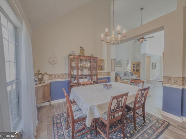 dining room featuring light wood-type flooring, ceiling fan with notable chandelier, and high vaulted ceiling