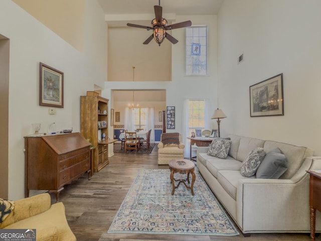 living room featuring hardwood / wood-style flooring, a towering ceiling, and ceiling fan with notable chandelier