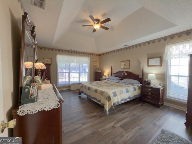 bedroom featuring ceiling fan, a textured ceiling, dark hardwood / wood-style flooring, and a tray ceiling