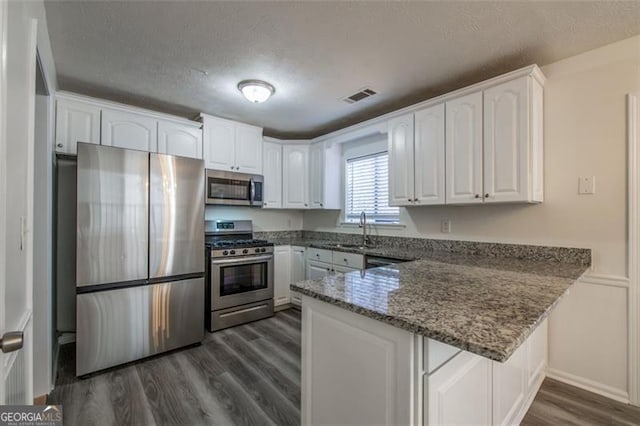 kitchen with sink, white cabinetry, dark stone countertops, stainless steel appliances, and kitchen peninsula