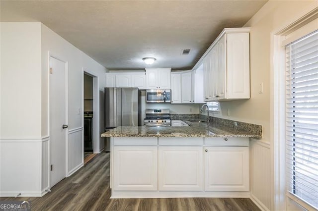 kitchen with sink, stone counters, white cabinetry, stainless steel appliances, and kitchen peninsula