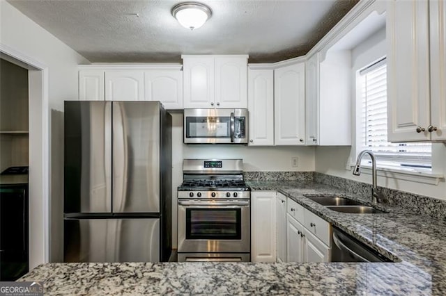 kitchen with sink, appliances with stainless steel finishes, a textured ceiling, white cabinets, and dark stone counters