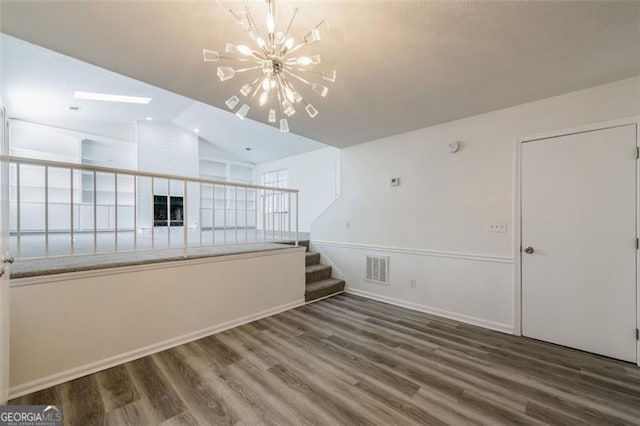 empty room with dark wood-type flooring, lofted ceiling, and a chandelier