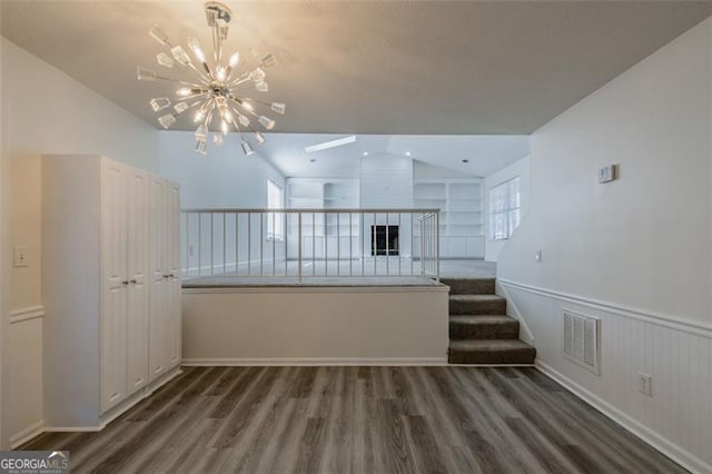 unfurnished living room featuring vaulted ceiling, dark wood-type flooring, and an inviting chandelier