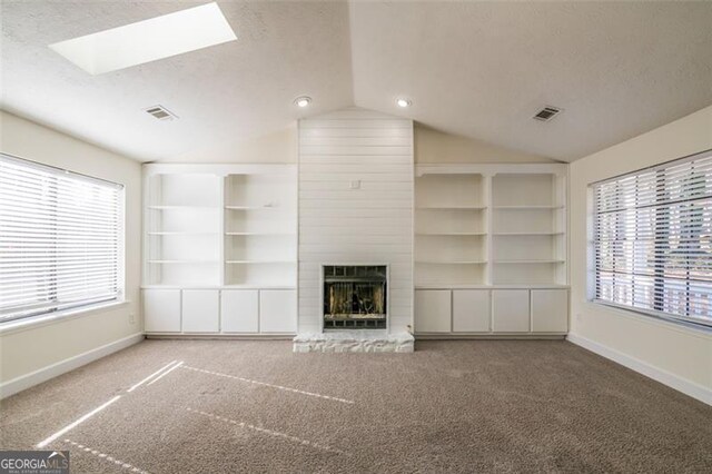 unfurnished living room with built in features, lofted ceiling with skylight, carpet floors, a fireplace, and a textured ceiling