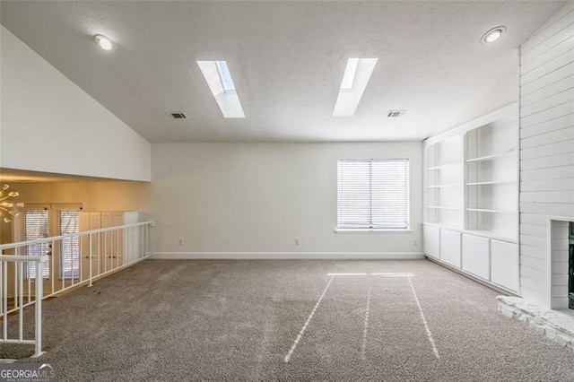 unfurnished living room featuring built in shelves, lofted ceiling with skylight, a textured ceiling, and carpet