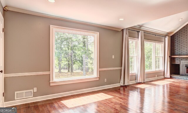 unfurnished living room with wood-type flooring, plenty of natural light, ornamental molding, and a fireplace