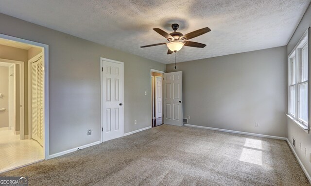 unfurnished bedroom featuring a textured ceiling, ensuite bath, ceiling fan, and carpet flooring