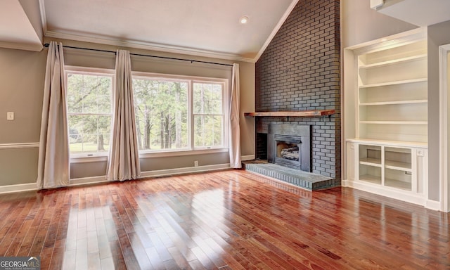 unfurnished living room featuring ornamental molding, lofted ceiling, hardwood / wood-style floors, and a brick fireplace