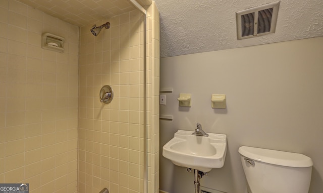 bathroom featuring sink, a tile shower, and toilet