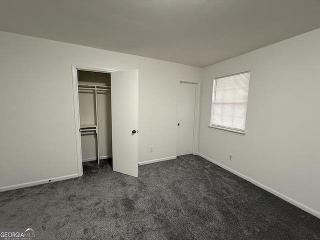 unfurnished bedroom with a closet and dark colored carpet