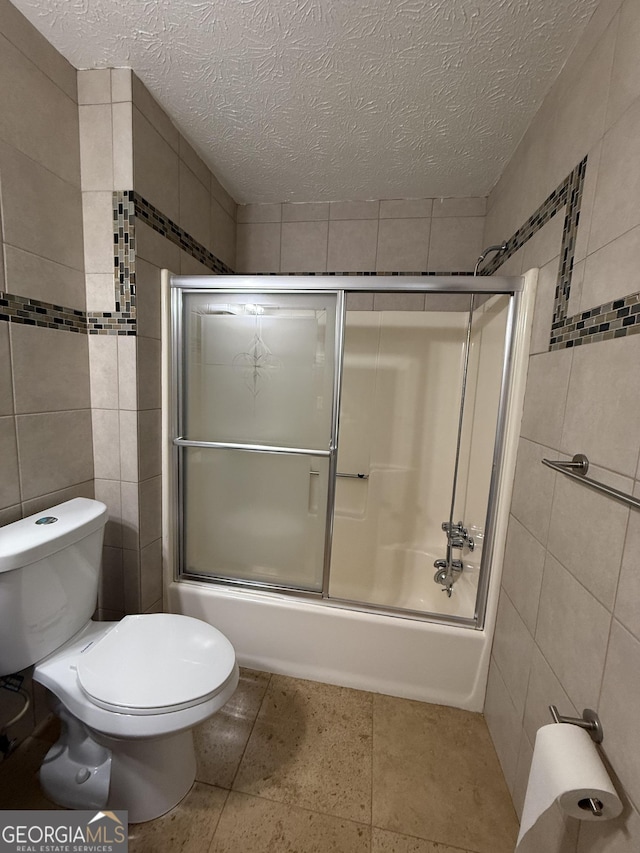 bathroom featuring bath / shower combo with glass door, tile walls, a textured ceiling, and toilet