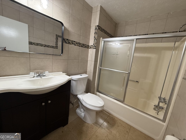 full bathroom featuring tile walls, enclosed tub / shower combo, vanity, toilet, and a textured ceiling