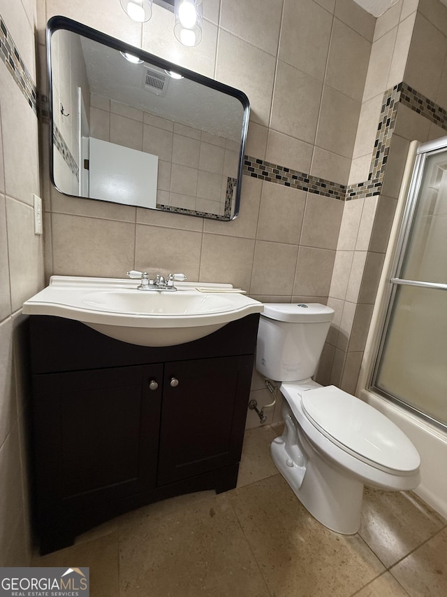 full bathroom featuring vanity, toilet, tile walls, and bath / shower combo with glass door