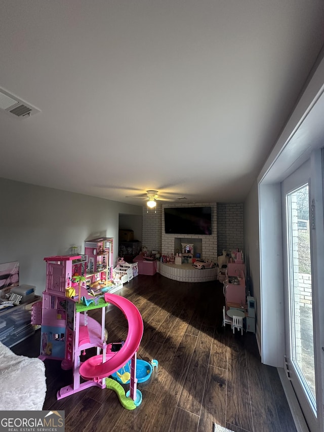 playroom with ceiling fan, brick wall, and dark hardwood / wood-style floors