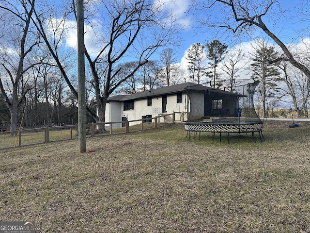 back of house with a trampoline and a yard