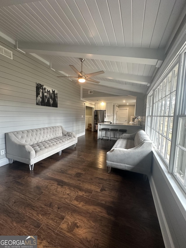 living room with ceiling fan, wood walls, vaulted ceiling with beams, and dark hardwood / wood-style floors