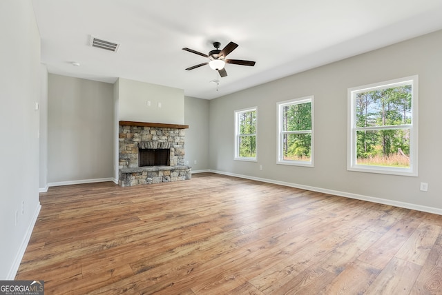 unfurnished living room featuring ceiling fan, light hardwood / wood-style flooring, and a stone fireplace