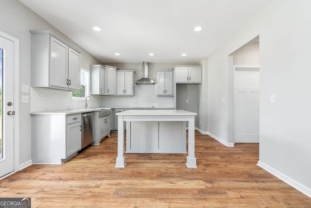 kitchen featuring dishwasher, wall chimney exhaust hood, light wood-type flooring, a kitchen island, and decorative backsplash