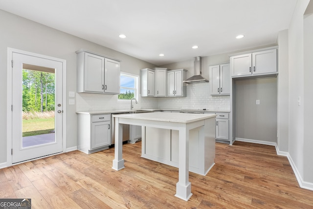 kitchen featuring a kitchen island, light hardwood / wood-style flooring, dishwasher, and wall chimney range hood