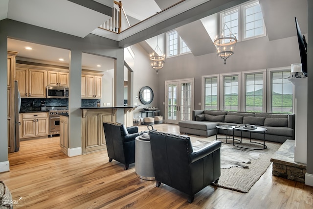 living room with a notable chandelier, a towering ceiling, french doors, and light hardwood / wood-style flooring