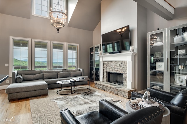 living room with hardwood / wood-style flooring, a stone fireplace, an inviting chandelier, and a towering ceiling