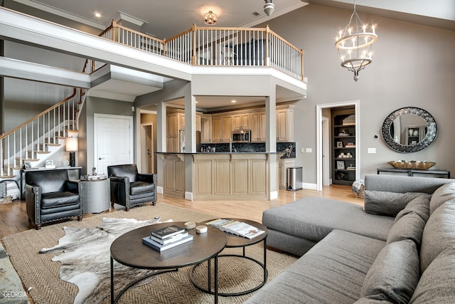 living room with a chandelier, ornamental molding, a towering ceiling, and light wood-type flooring