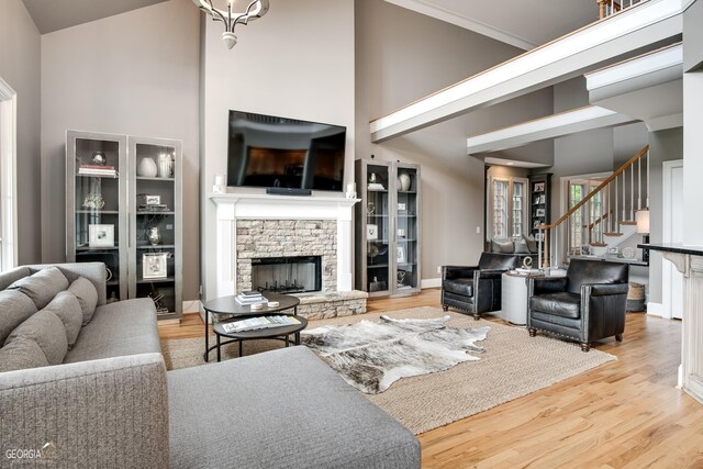 living room featuring light hardwood / wood-style floors, a towering ceiling, and a stone fireplace